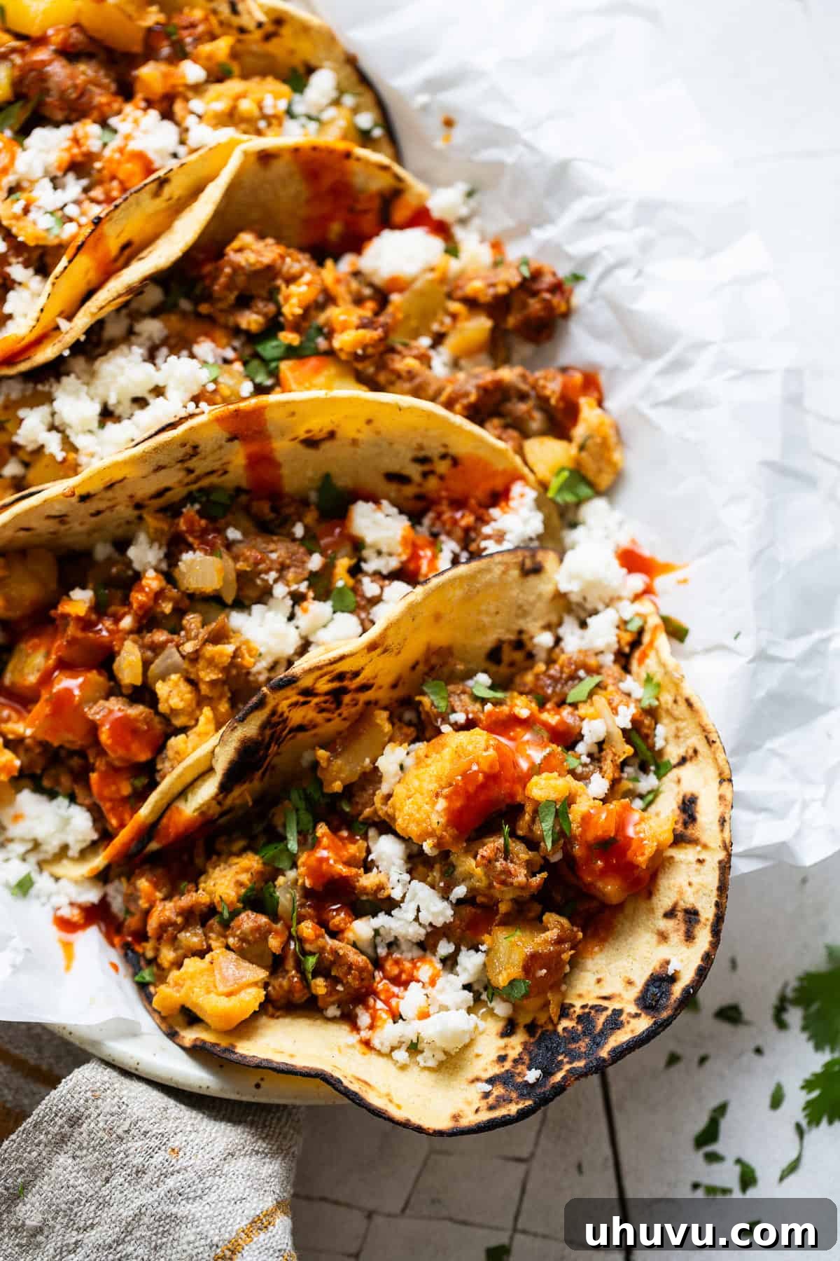 Morning Taco Bliss 6 Fully assembled breakfast tacos, garnished with fresh cilantro, spicy hot sauce, and crumbled queso fresco, ready to be enjoyed.