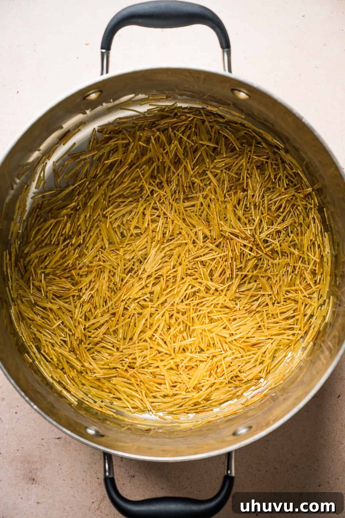 Close-up of fideo noodles being toasted to a golden brown in a large pot with olive oil, developing a rich, nutty flavor.