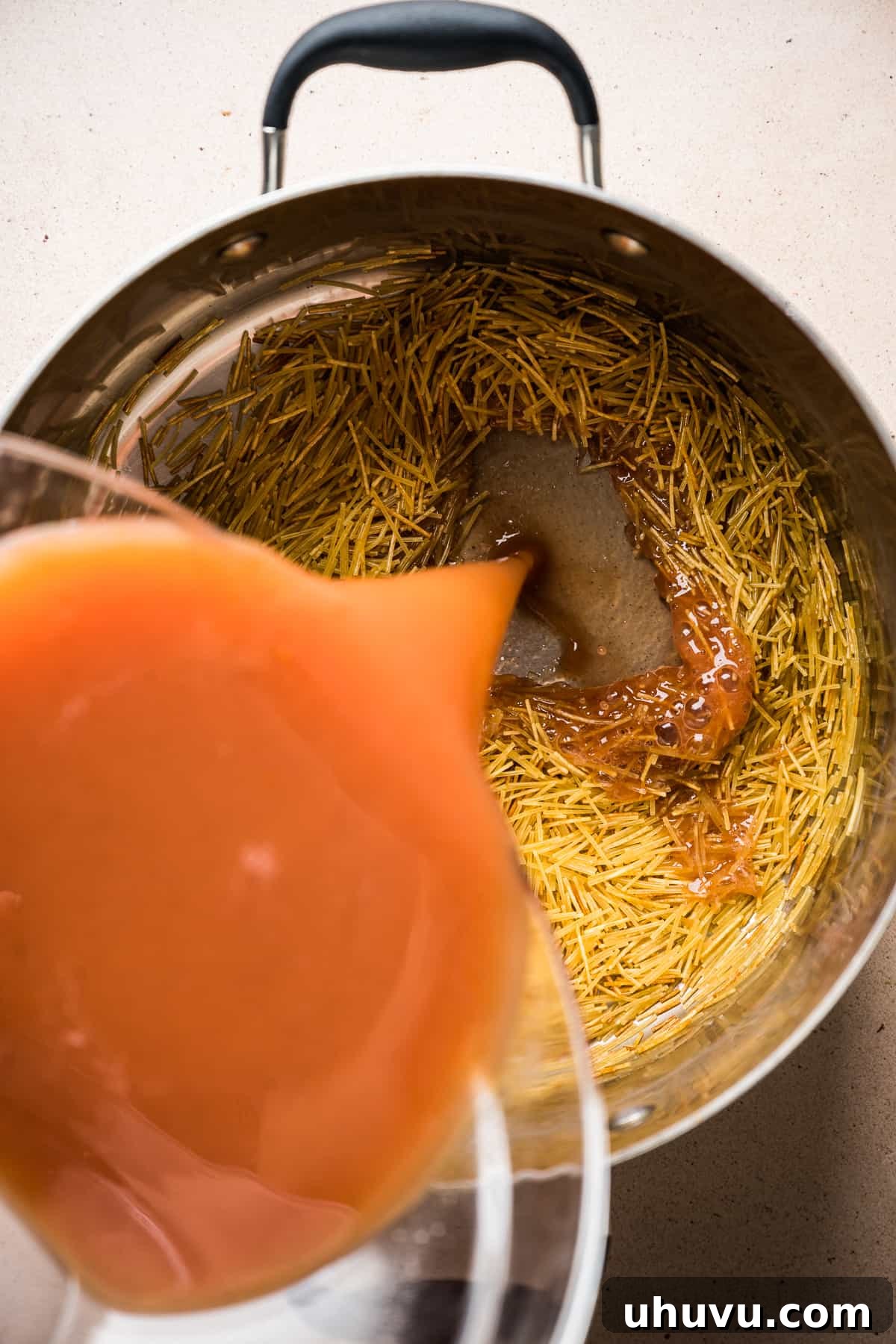Rich tomato broth being poured into a pot of beautifully toasted fideo noodles, ready to simmer into a comforting Sopa de Fideo.