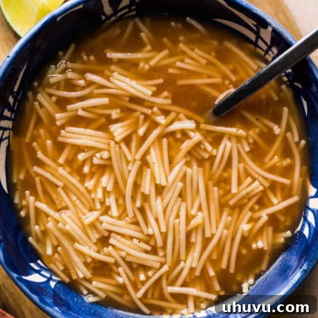 Sopa de Fideo (Mexican noodle soup) in a bowl ready to eat, garnished with cilantro and lime.