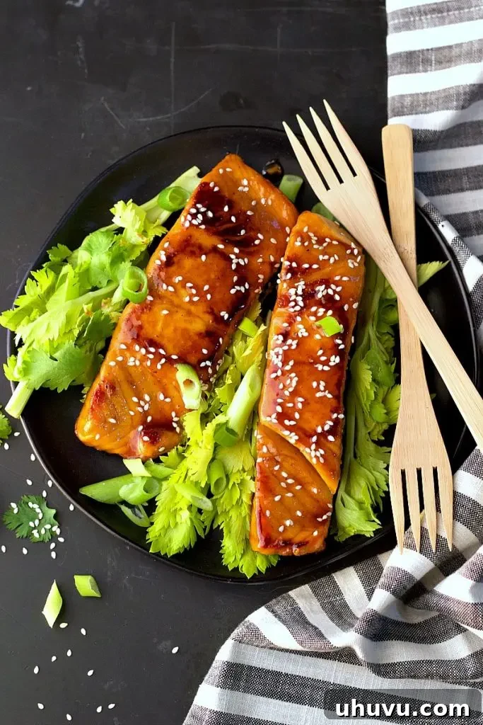 Asian teriyaki salmon served on a black plate with fresh green vegetables