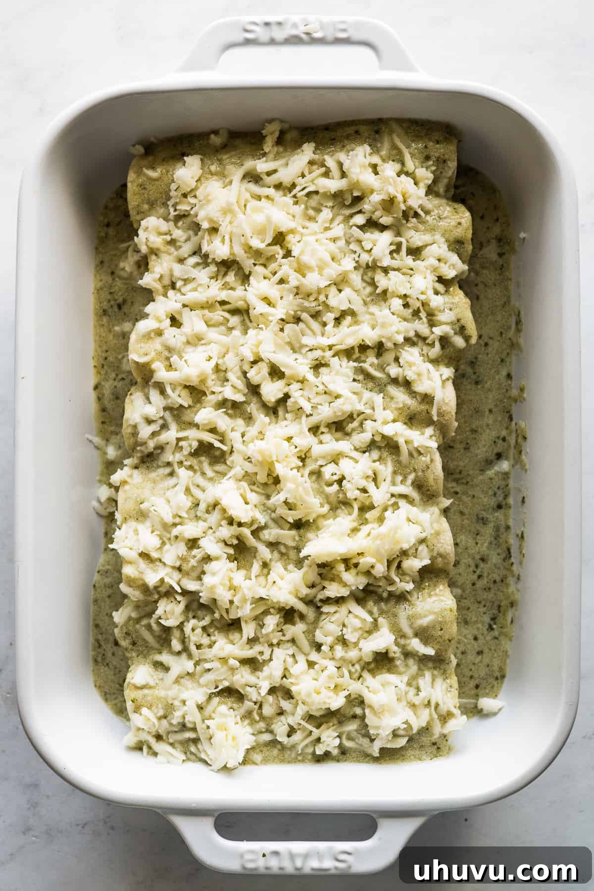 Creamy Tomatillo Enchiladas 7 Enchiladas suizas topped with shredded Chihuahua cheese in a baking dish.