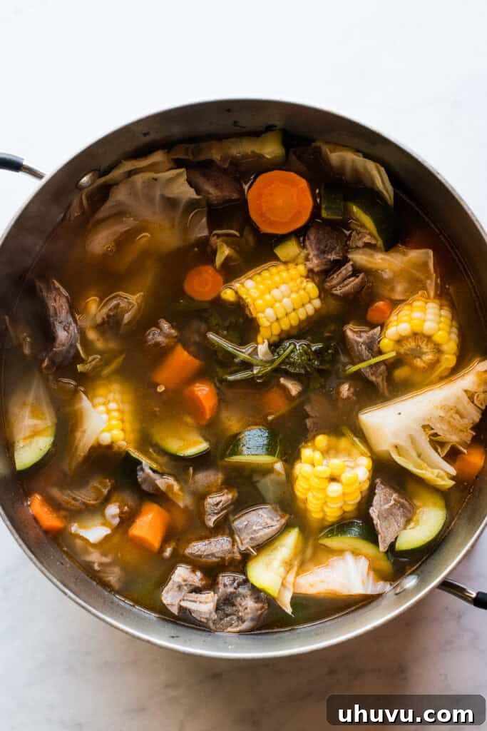 Heartwarming Beef and Vegetable Soup 8 A bowl of Caldo de Res being garnished with fresh cilantro, a lime wedge, and a dash of hot sauce.