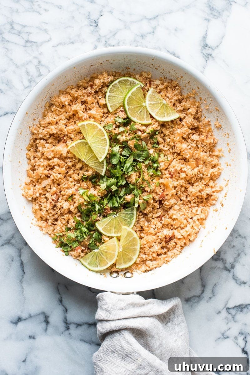 Fiesta Cauliflower Rice 2 Mexican cauliflower rice in a large skillet garnished with cilantro and lime wedges.