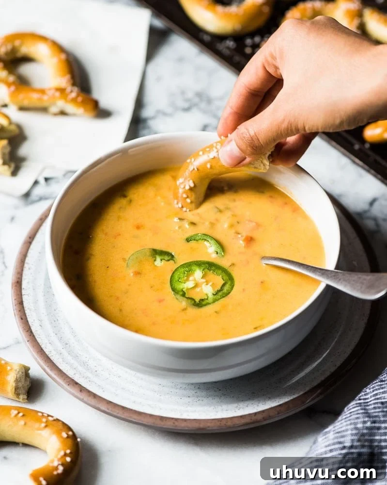 Golden Ale and Sharp Cheddar Bisque 7 Beer cheese soup in a white bowl topped with thinly sliced fresh jalapenos.