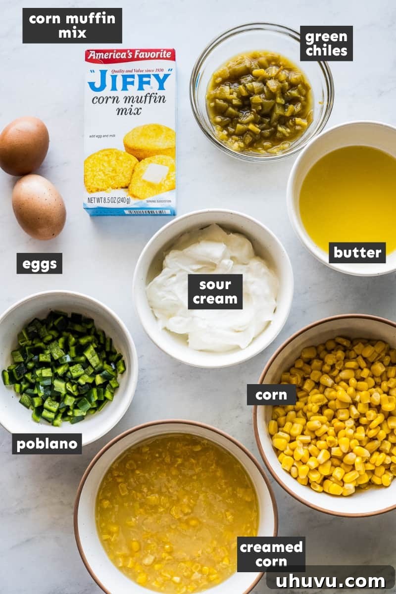 Zesty Green Chili Corn Bake 3 Ingredients for Green Chili Corn Casserole laid out on a wooden table, including cans of corn, sour cream, butter, eggs, peppers, Jiffy mix, and cheese.