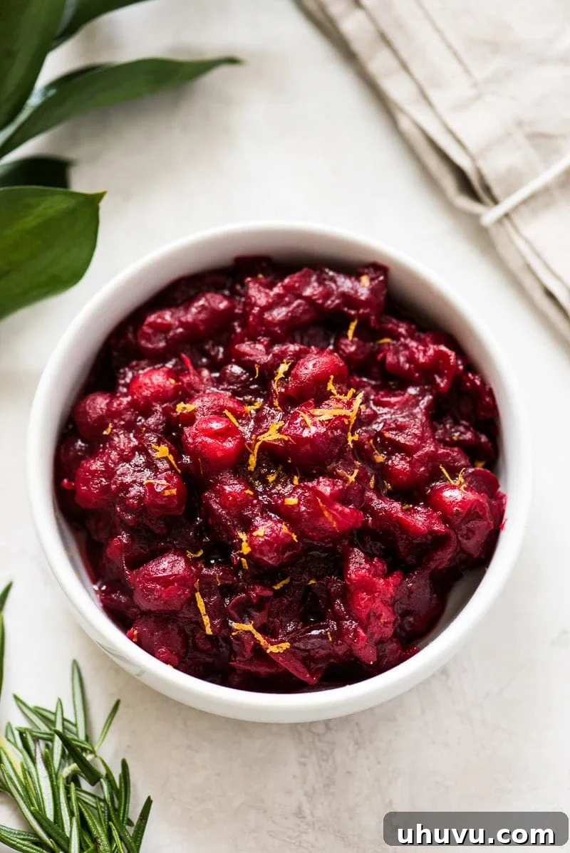 A cranberry sauce recipe in a white bowl topped with orange zest, perfect for holiday meals.