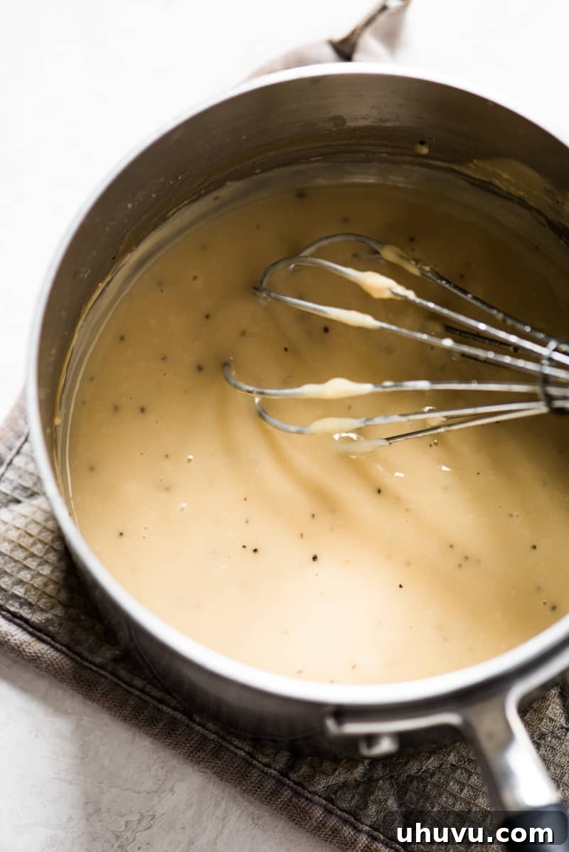 Perfect Turkey Gravy from Pan Drippings 5 A rich, golden-brown turkey gravy being stirred with a whisk in a medium saucepan, highlighting its creamy texture.