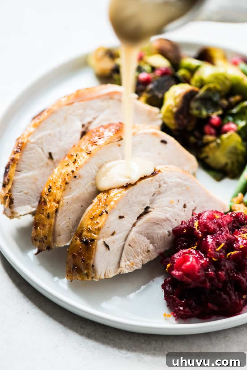 Perfect Turkey Gravy from Pan Drippings 6 Appetizing slices of roasted turkey on a white plate being generously covered with a stream of golden-brown homemade turkey gravy, ready for serving.