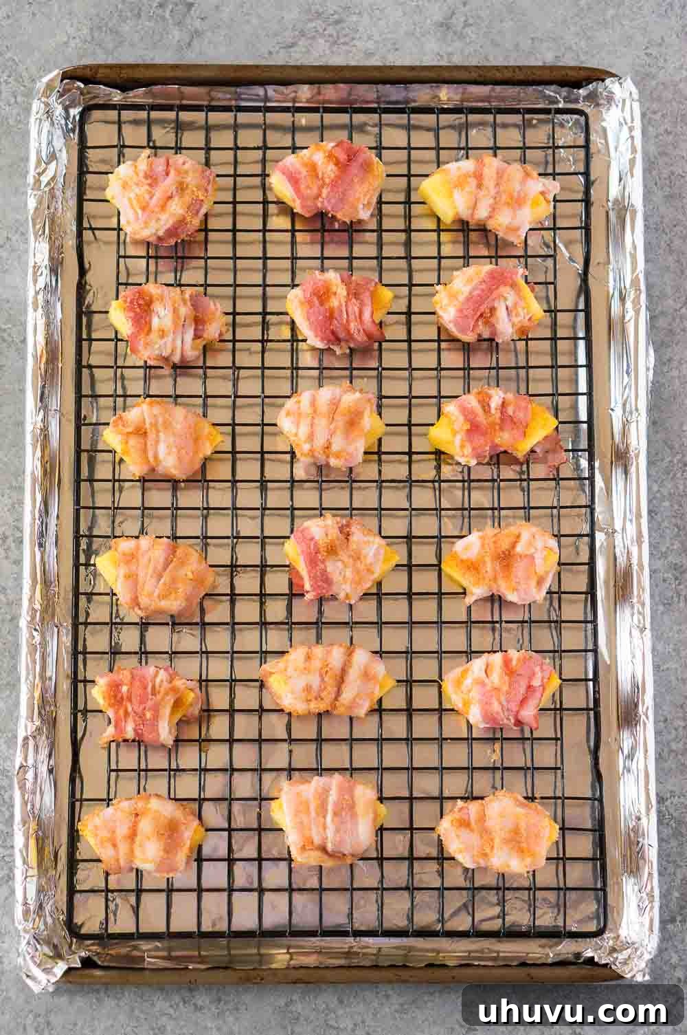 Sweet & Savory Bacon Pineapple Poppers 6 Bacon wrapped pineapple bites arranged on a baking sheet before cooking