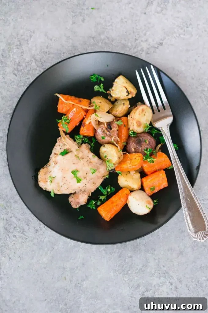 Roasted chicken, potatoes, and carrots on a dark baking sheet, ready to serve.