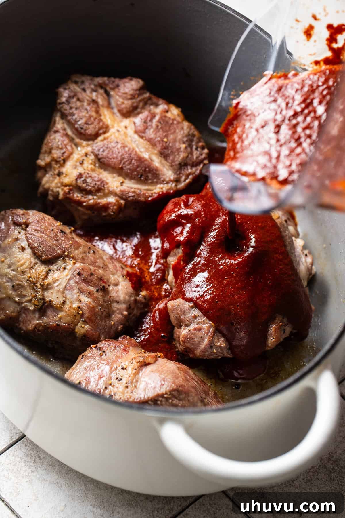 The rich, vibrant red chile broth being carefully poured over the seared pork chunks in a large pot, ready to simmer and transform into a delicious pozole rojo.