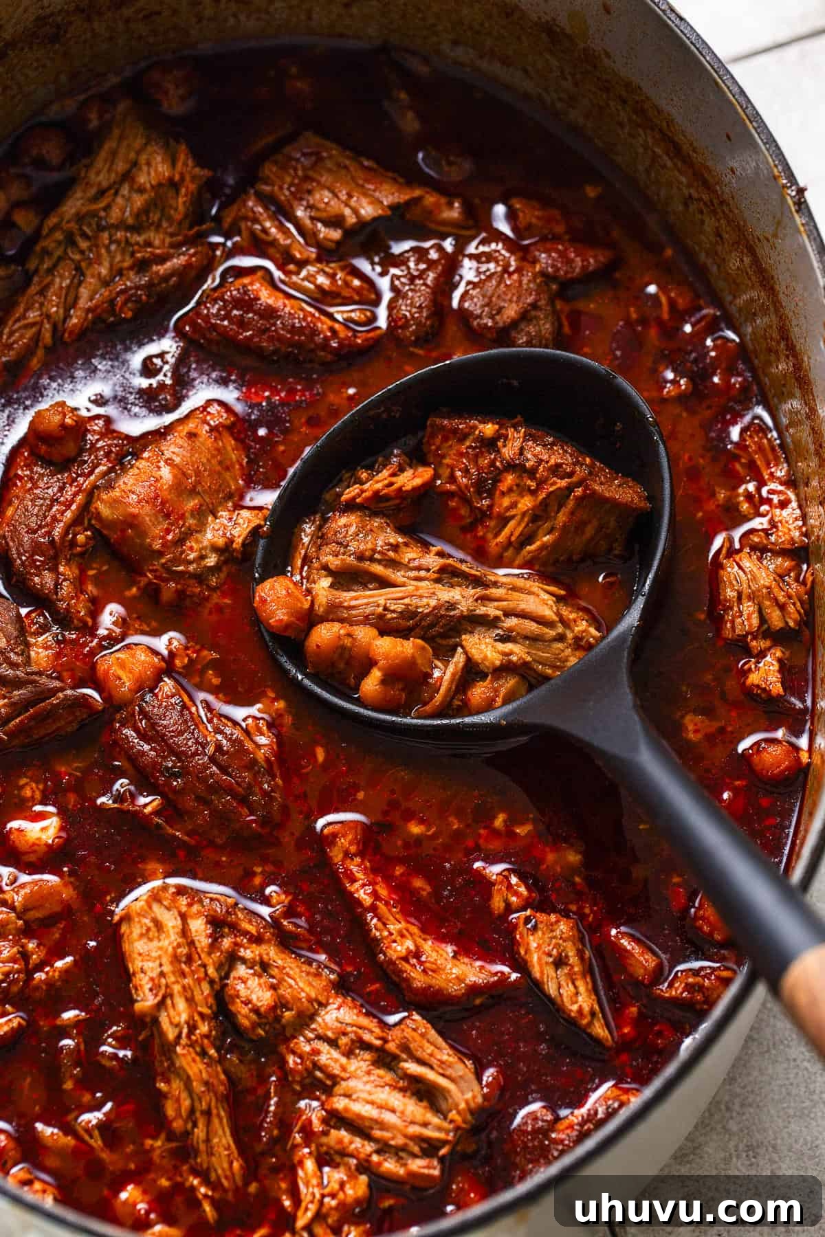 A large pot of perfectly cooked Mexican pozole rojo, with tender shredded pork and plump hominy swimming in a rich red chile broth, emitting steam and ready to be served.