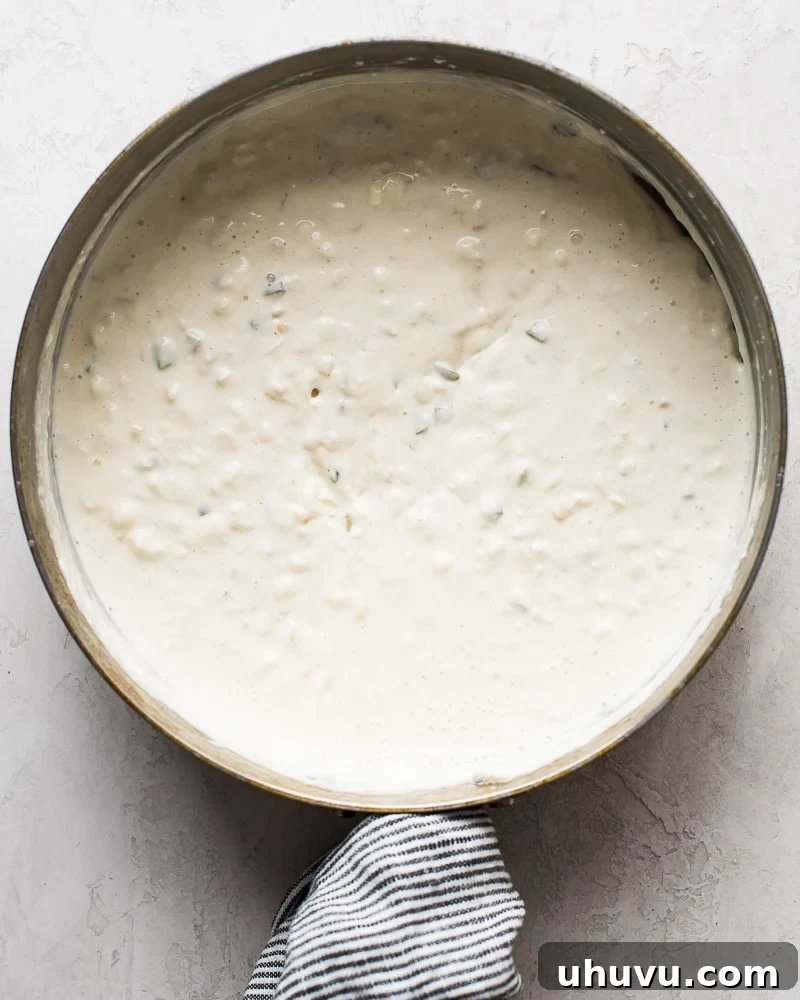 Quick Creamy Queso 4 The process of adding milk and cream cheese to the sautéed vegetables, stirring to create a smooth base for the queso.