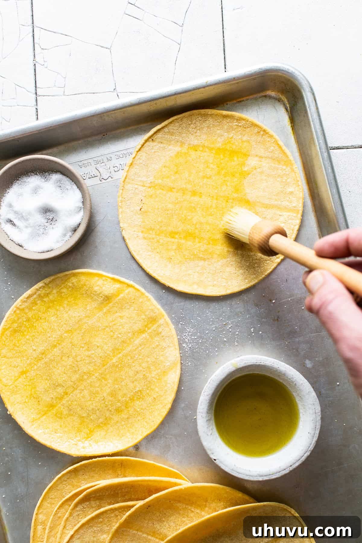 Golden Tostada Crisps 4 Brushing oil on both sides of a corn tortilla on top of a baking sheet, preparing it for baking.