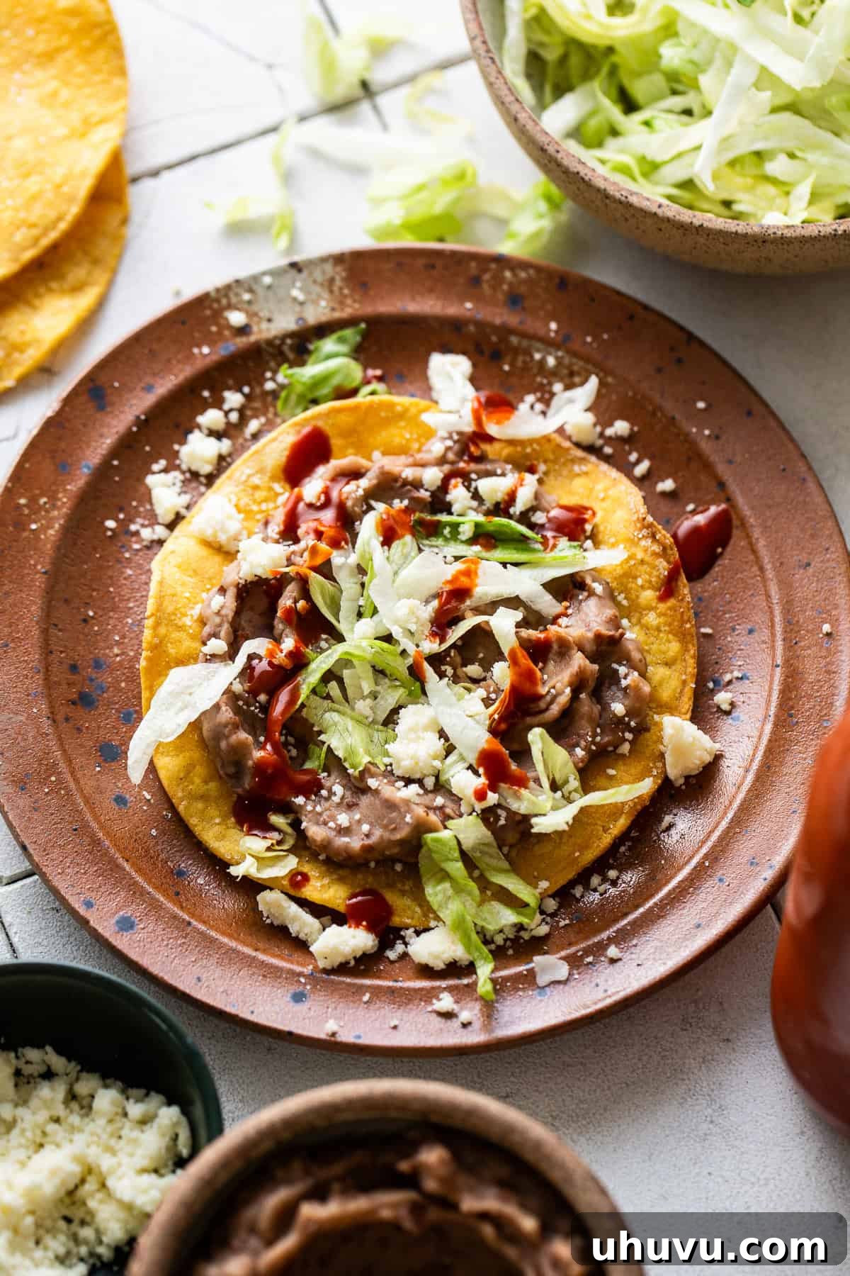 Golden Tostada Crisps 7 A perfectly assembled tostada shell topped with creamy refried beans, crisp lettuce, shredded cheese, and vibrant salsa, ready for a delicious bite.
