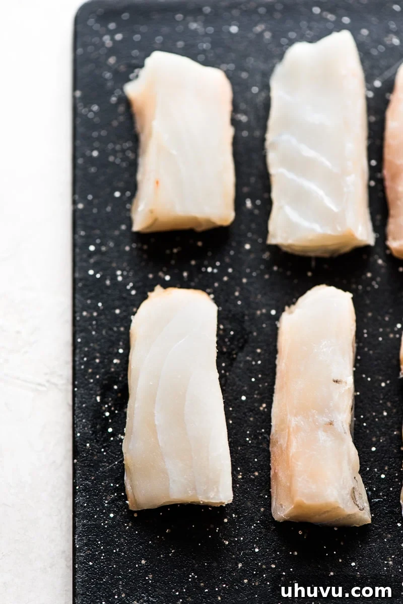 Golden Crispy Baja Fish Tacos 6 Sliced strips of Atlantic Cod on a black cutting board, neatly prepared for a Baja Fish Tacos recipe.