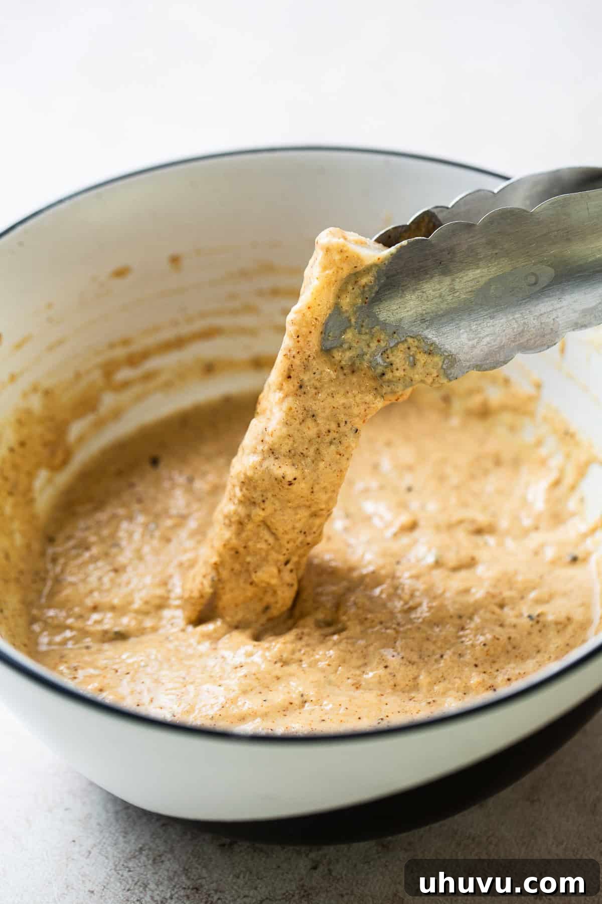 Golden Crispy Baja Fish Tacos 9 A piece of fish being carefully dipped into the airy beer batter, ensuring a full coating for crispiness.