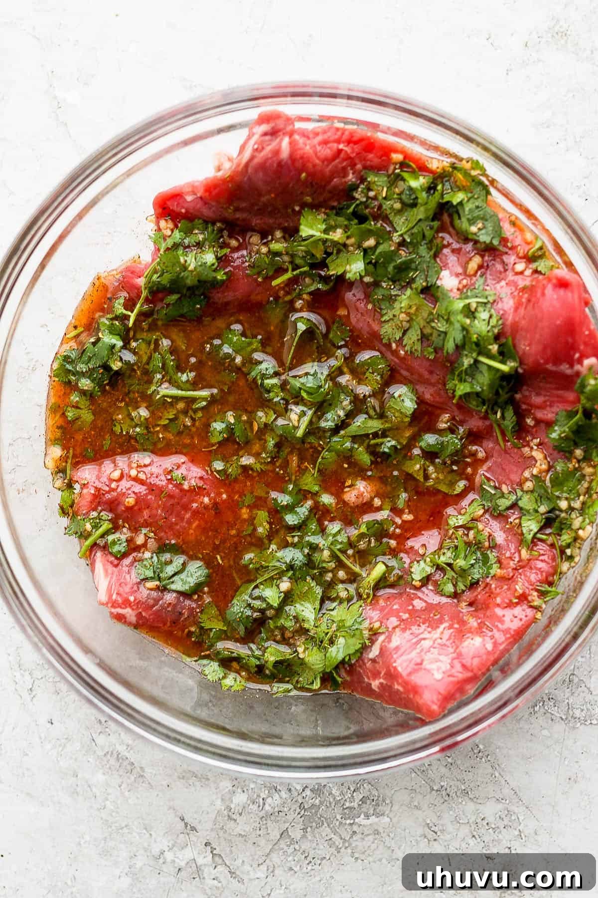 Raw flank steak marinating in a bowl.
