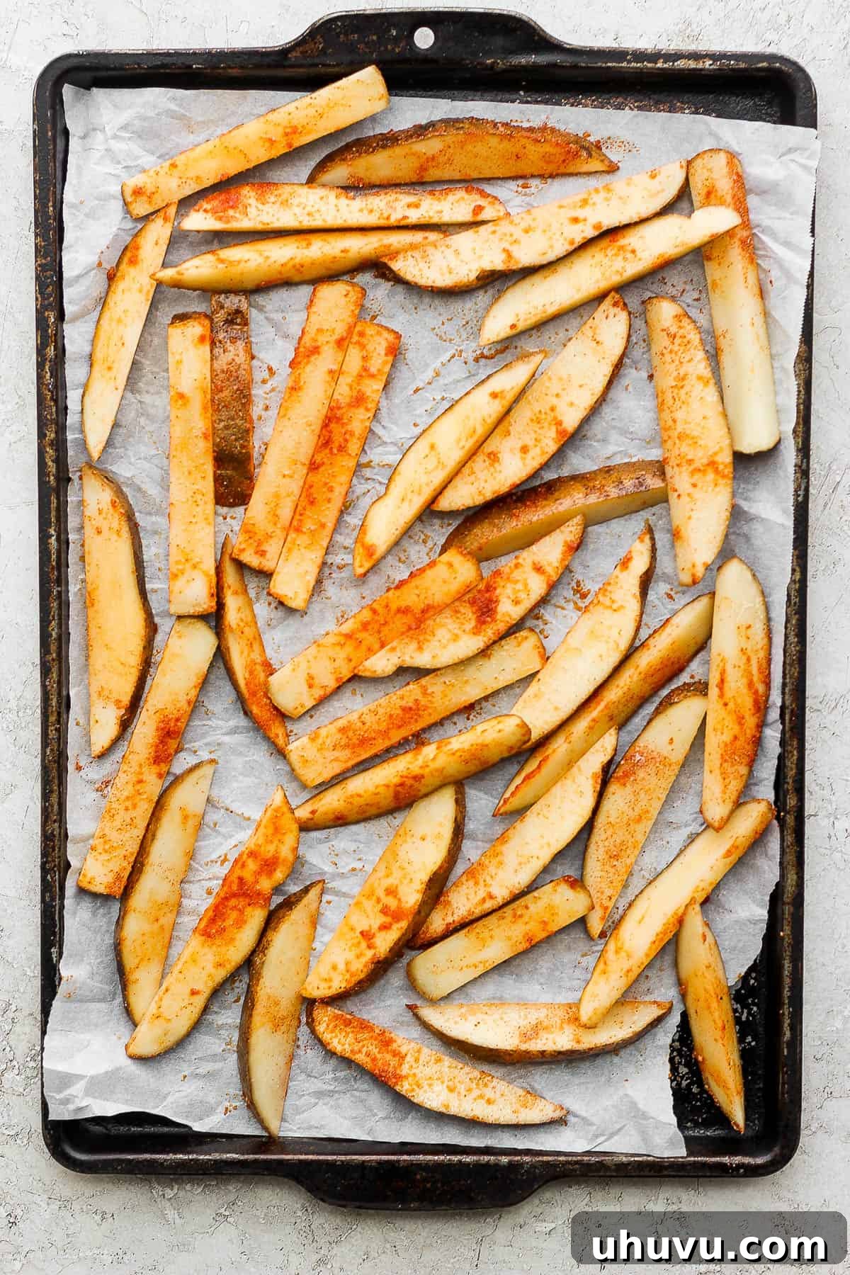 Potato fries sliced, seasoned, and placed on a large baking sheet lined with parchment paper. 