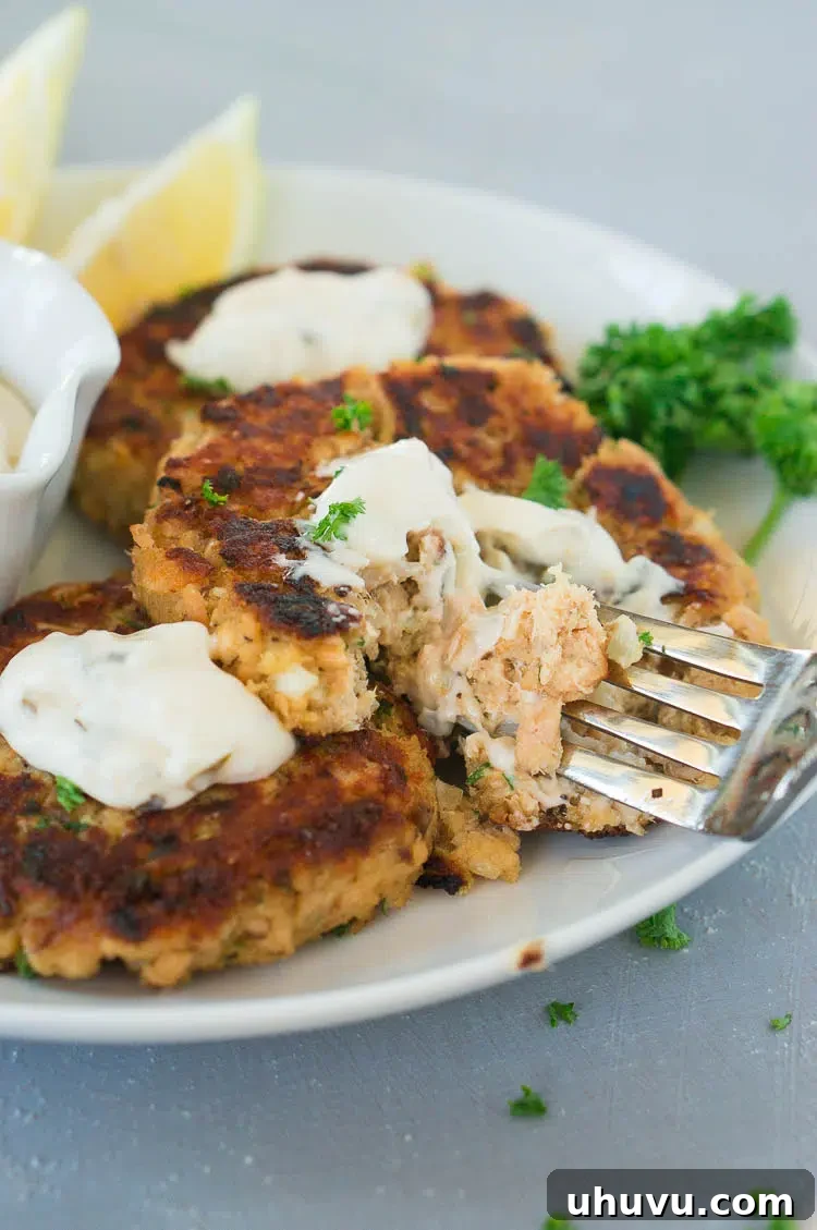 A fork taking a delicious bite from a golden-brown salmon fish cake, showcasing its flaky texture and tempting appeal.