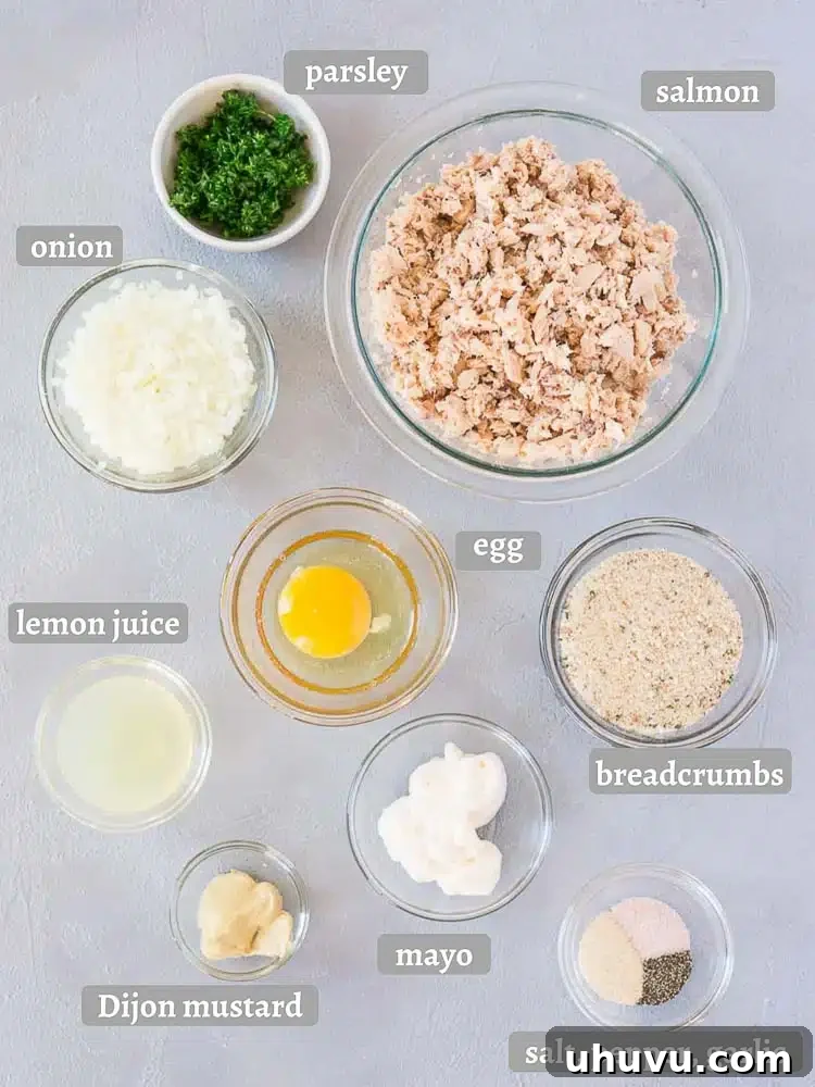 A rustic gray board displaying all the fresh ingredients needed to make salmon patties, including salmon, lemon, parsley, and various seasonings.