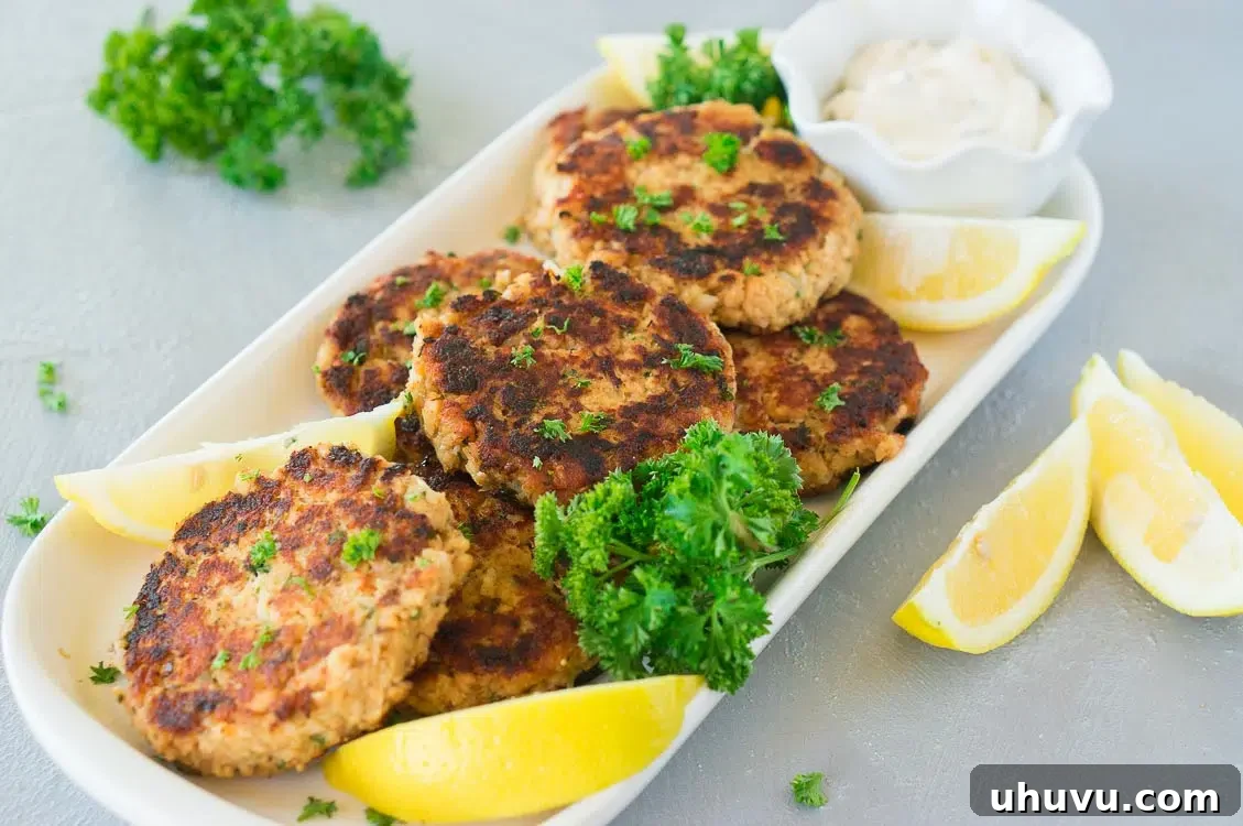 A close-up shot of perfectly cooked salmon patties, garnished with fresh lemon wedges and a small bowl of creamy tartar sauce, on a rustic serving platter.