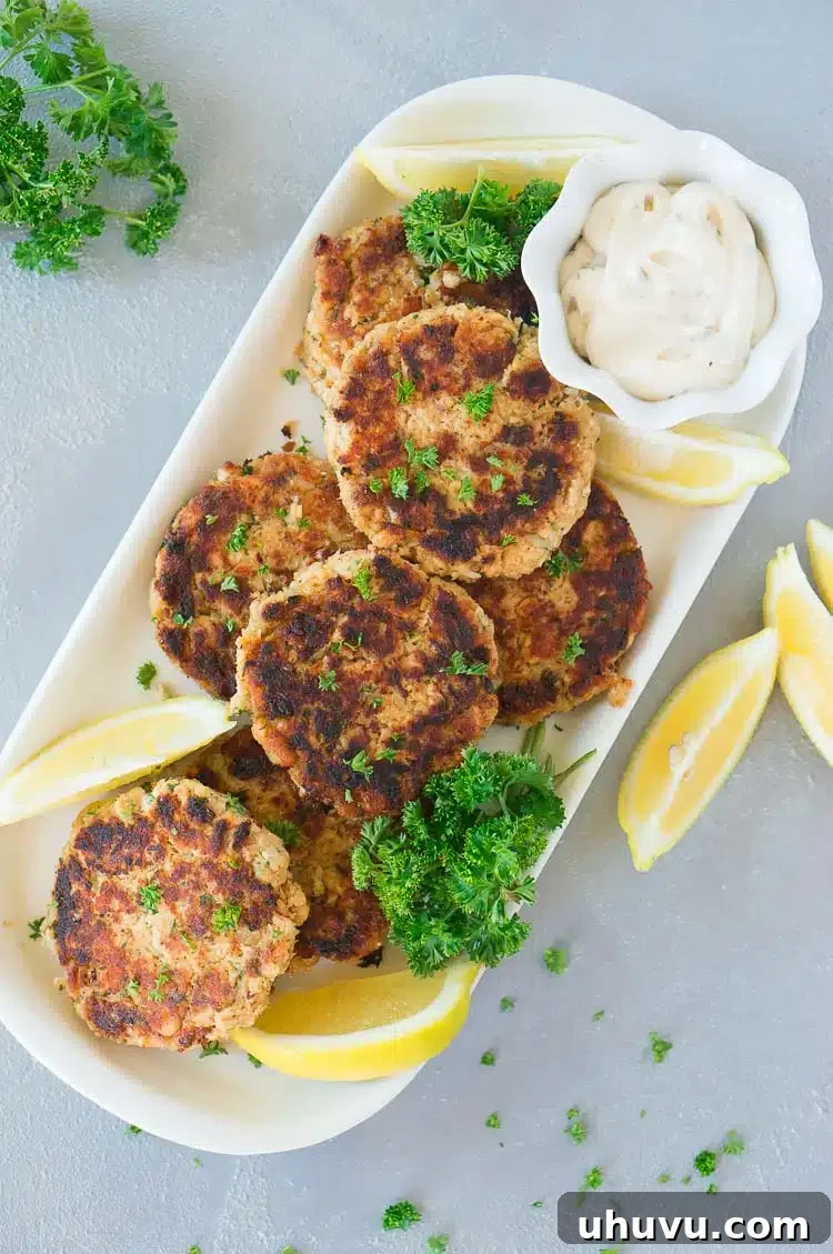 The best salmon patties beautifully plated on a wooden board, accompanied by fresh lemon wedges, creamy tartar sauce, and a sprig of parsley, highlighting their freshness and appeal.