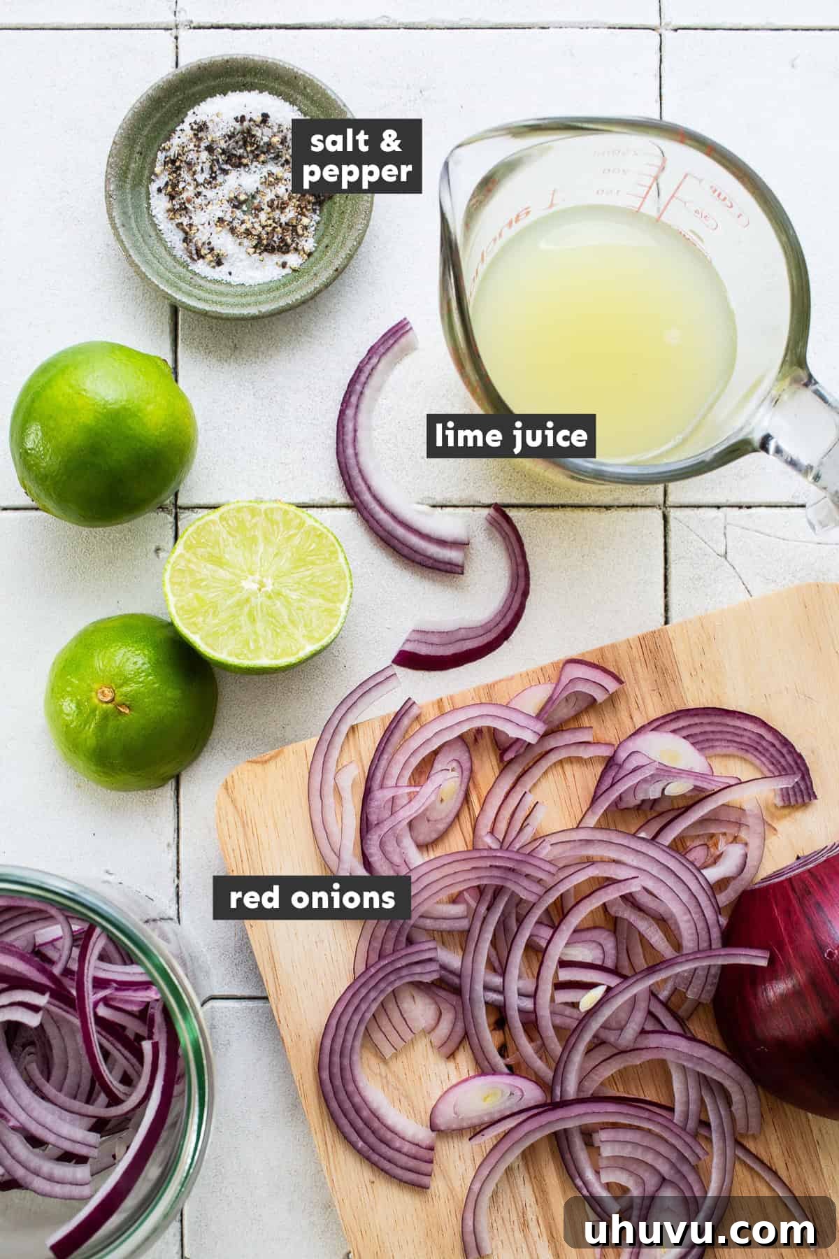 Tangy Mexican Ruby Rings 3 A selection of ingredients for Mexican Pickled Onions displayed on a rustic wooden table, including thinly sliced red onions, fresh limes, kosher salt, and black peppercorns.