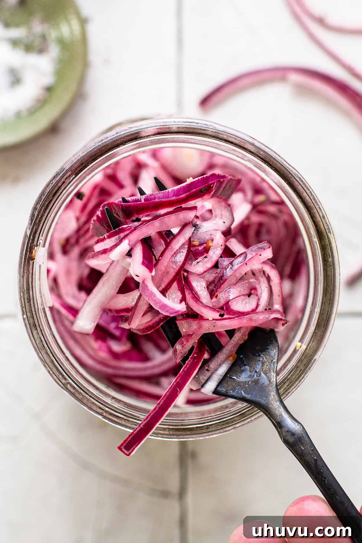 A glass jar filled with vibrant pink Mexican pickled onions, with a fork lifting some out, ready to be enjoyed.