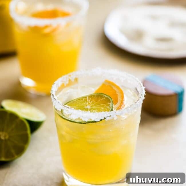 Skinny margarita cocktail glass garnished with sliced lime and orange.