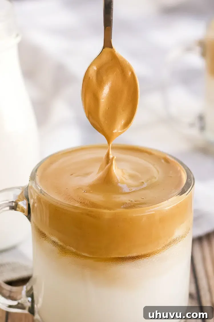 Close-up of whipped Dalgona coffee foam in a clear mug, showing its rich texture