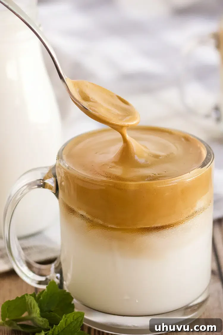 Spooning whipped Dalgona coffee over cold milk and ice in a glass