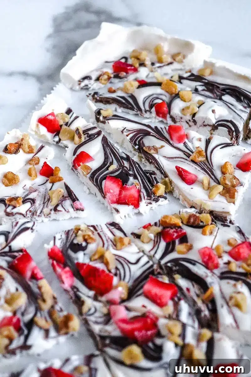 Refreshing Strawberry Frozen Yogurt Bark 7 Portioned pieces of keto frozen yogurt bark adorned with fresh strawberries and chocolate swirls, ready to serve.
