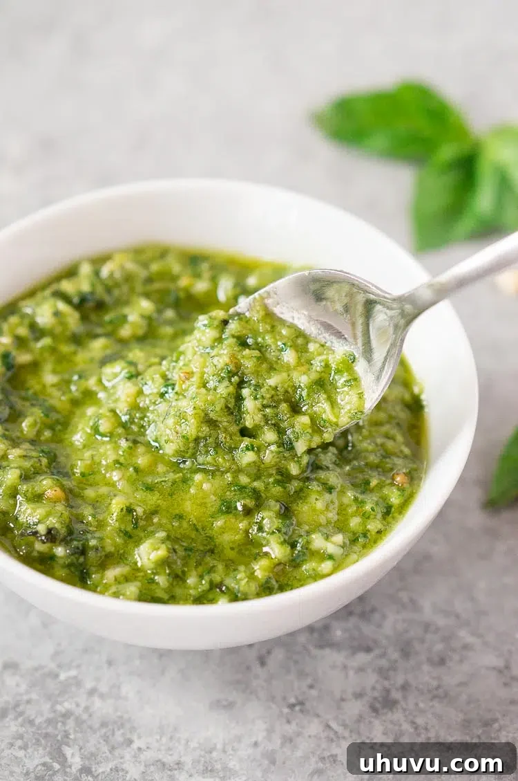 Creamy homemade pesto sauce in a white bowl with a spoon, highlighting its smooth texture