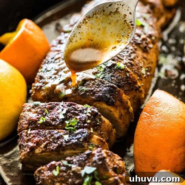 A spoon pouring citrus juices over roasted pork tenderloin in a black cast iron skillet.