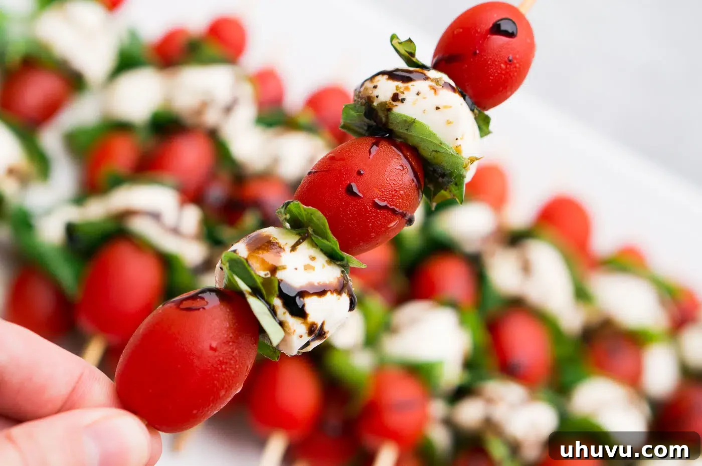 Close-up of a platter of individual Caprese skewers featuring tomatoes, fresh mozzarella, and basil