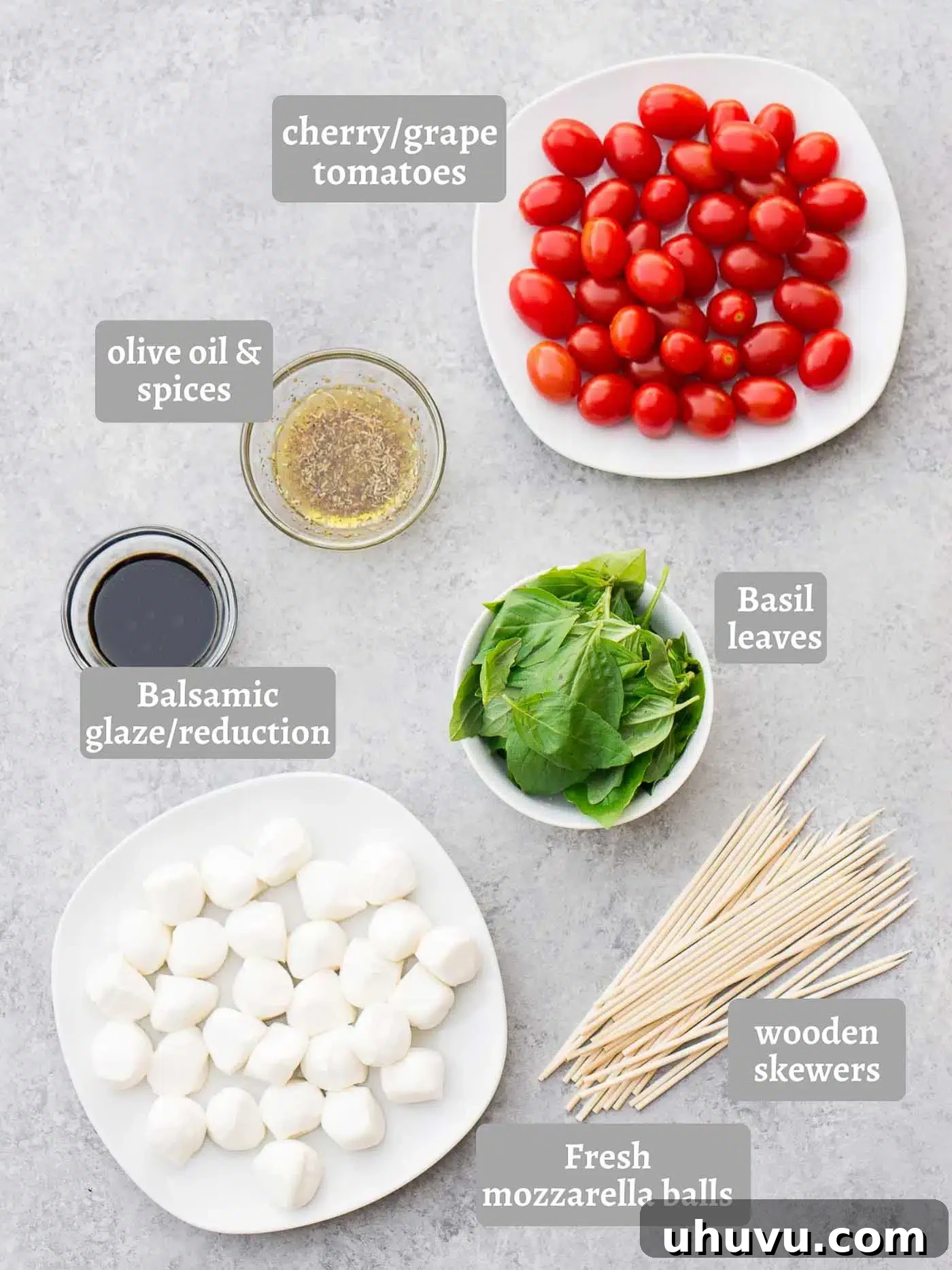 Assortment of fresh ingredients for Caprese skewers including cherry tomatoes, mozzarella balls, basil, and a bottle of olive oil