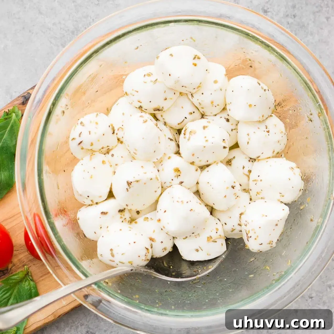 Fresh mozzarella balls marinating in olive oil and Italian herbs in a small white bowl