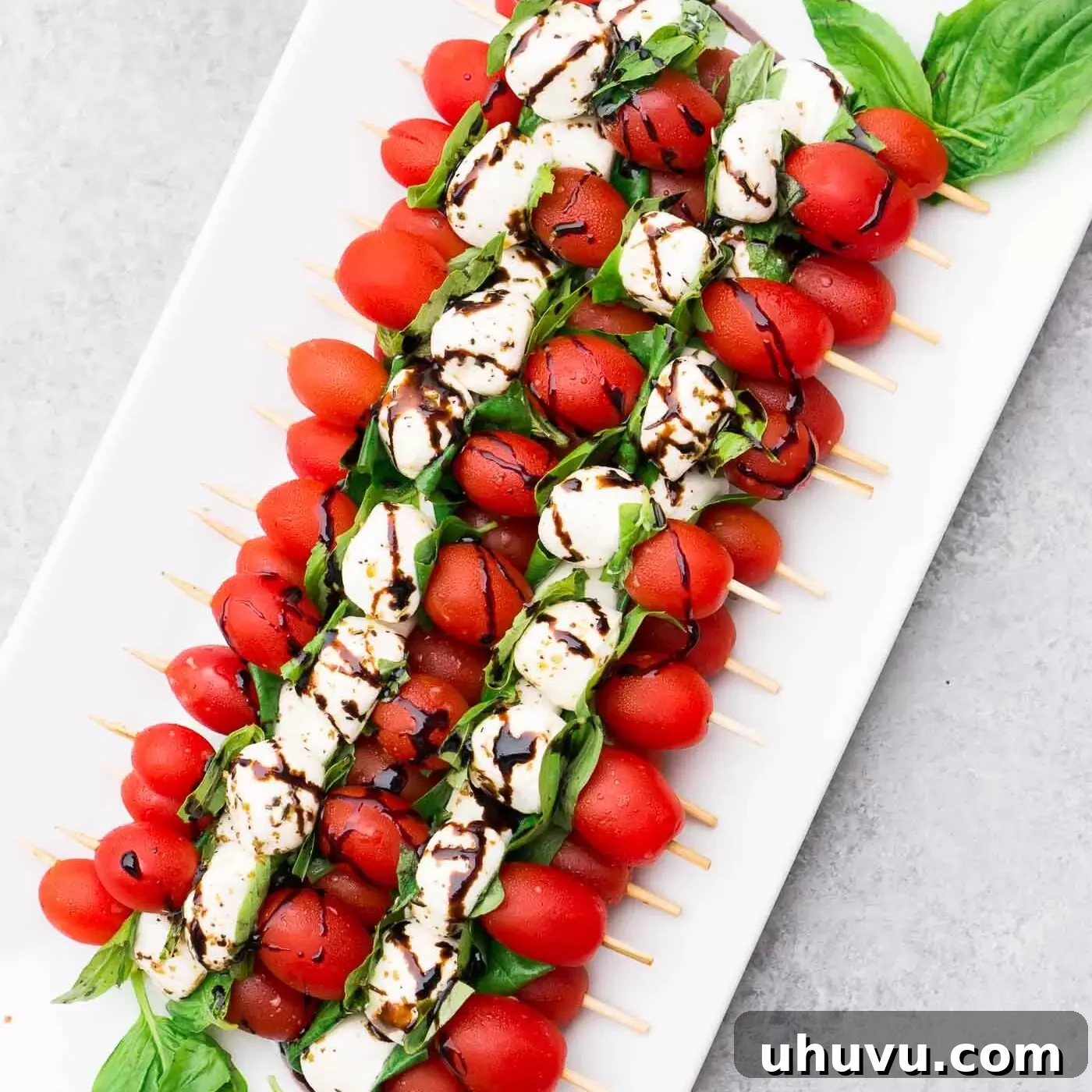 Finished Caprese skewers generously drizzled with rich balsamic glaze on a serving platter