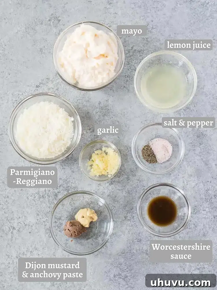 A beautiful flat lay of fresh ingredients laid out for making homemade Caesar dressing, including garlic, lemons, Dijon mustard, and Parmesan cheese.