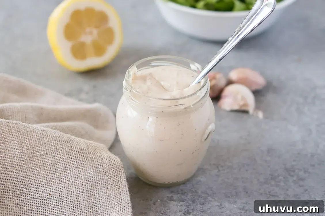 Homemade Caesar dressing stored in a glass jar, with fresh lemons and garlic cloves blurred in the background, hinting at fresh ingredients.