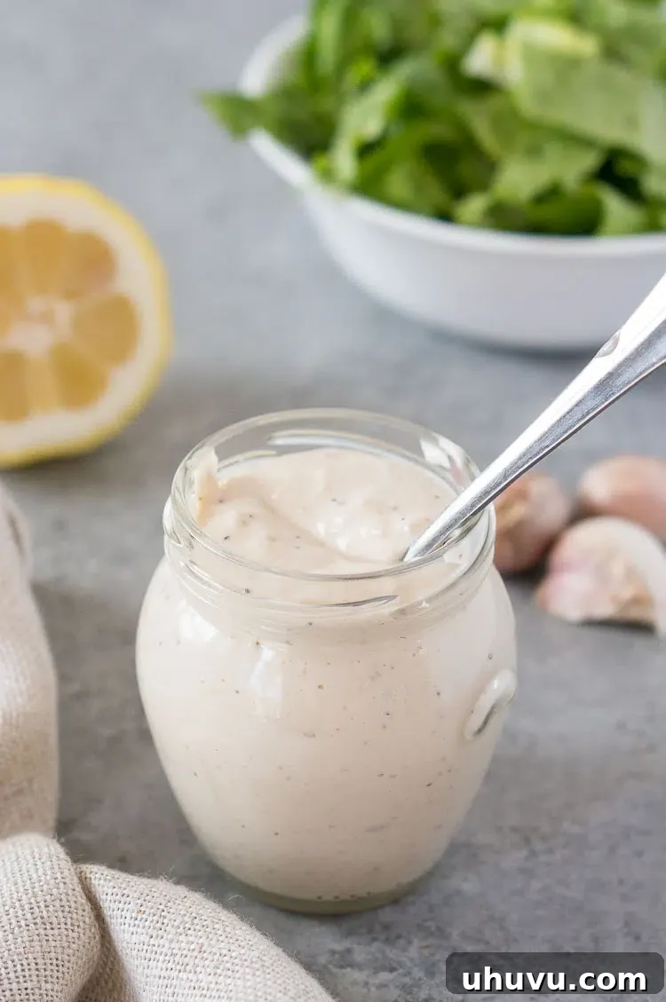A glass jar filled with healthy homemade Caesar salad dressing, with a spoon resting inside, ready for serving.