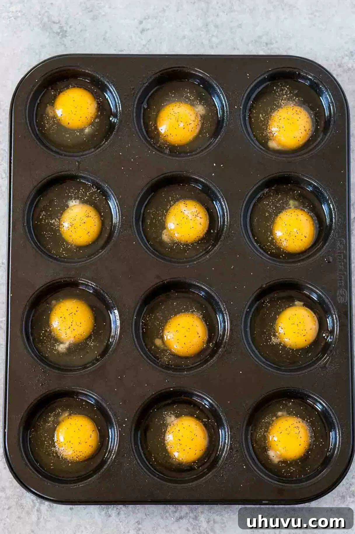 12 cracked eggs in a muffin tin with seasoning