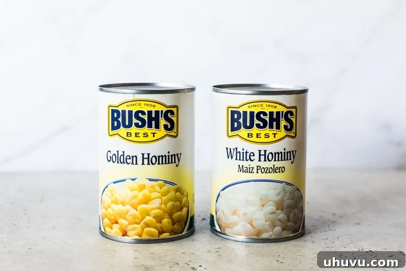 Two cans of different types of hominy. One is golden yellow hominy and one is white hominy, with fresh corn kernels scattered around.
