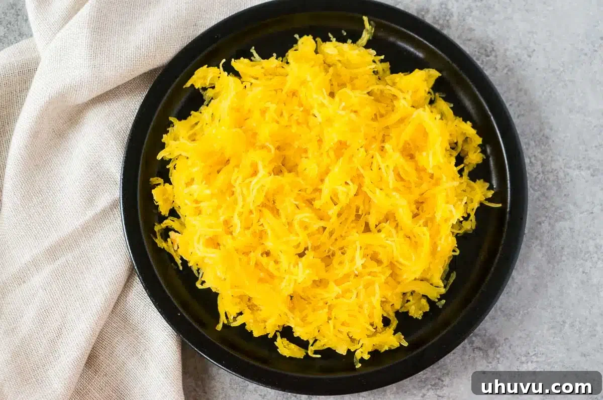 Cooked spaghetti squash in its shell on a black plate, ready to be scraped.