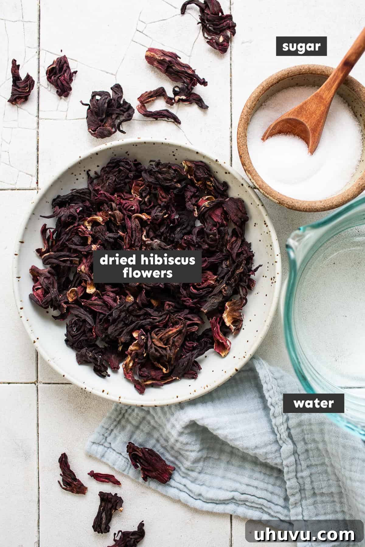 Ruby Hibiscus Refresher 3 Ingredients for making agua de jamaica drink laid out on a table, including dried hibiscus flowers, water, and sugar.