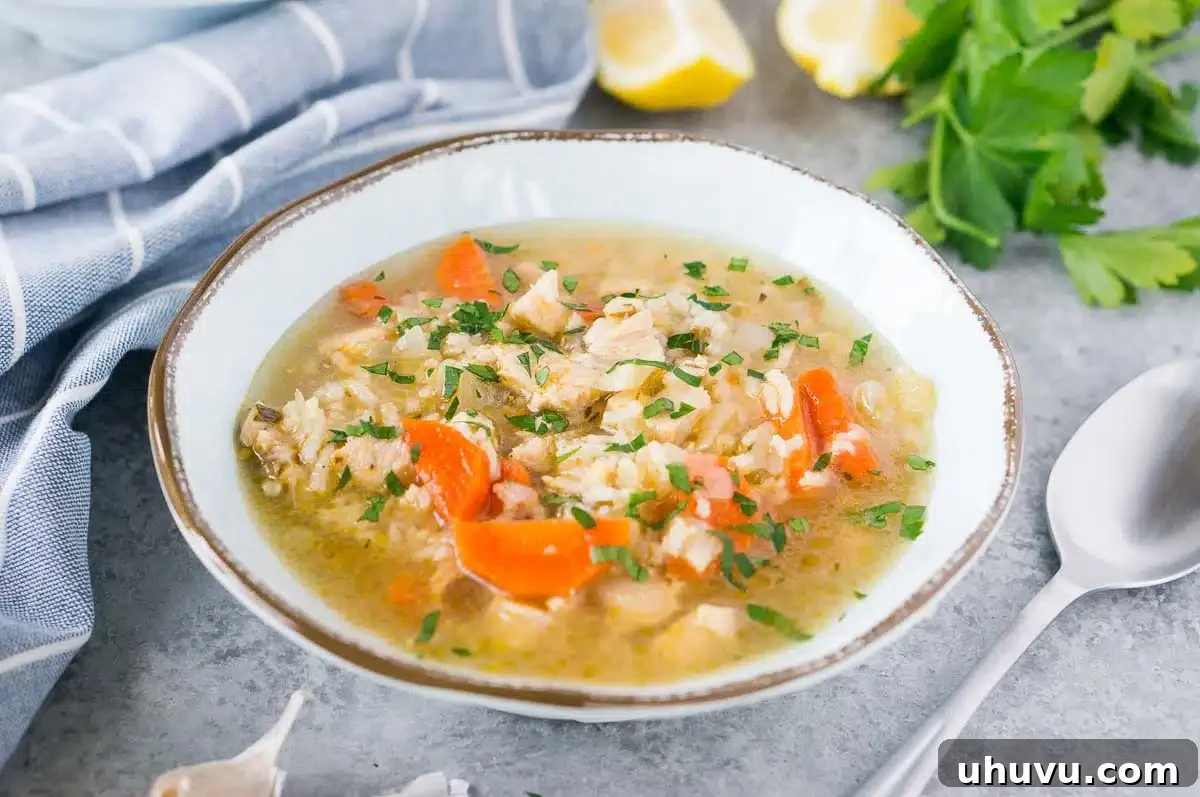 A steaming bowl of homemade turkey soup with rice, garnished with fresh parsley, served on a dark wooden surface