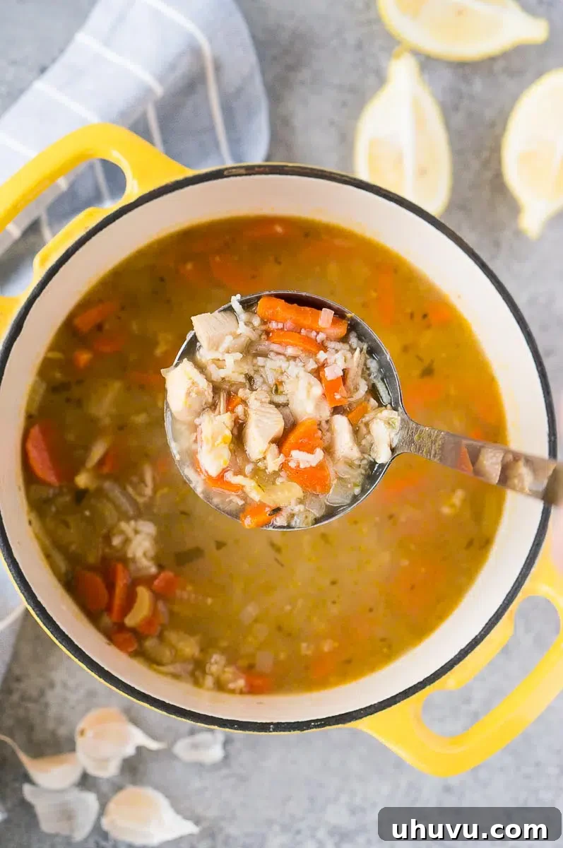 A ladle full of rich and hearty turkey rice soup, held above a large pot of simmering soup, showcasing its delicious texture