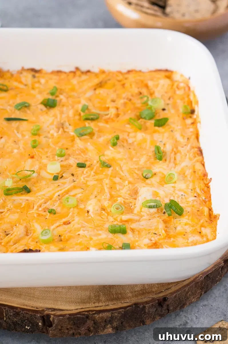 Close-up of creamy, golden buffalo chicken dip in a white dish, garnished with green onions and ready to be served